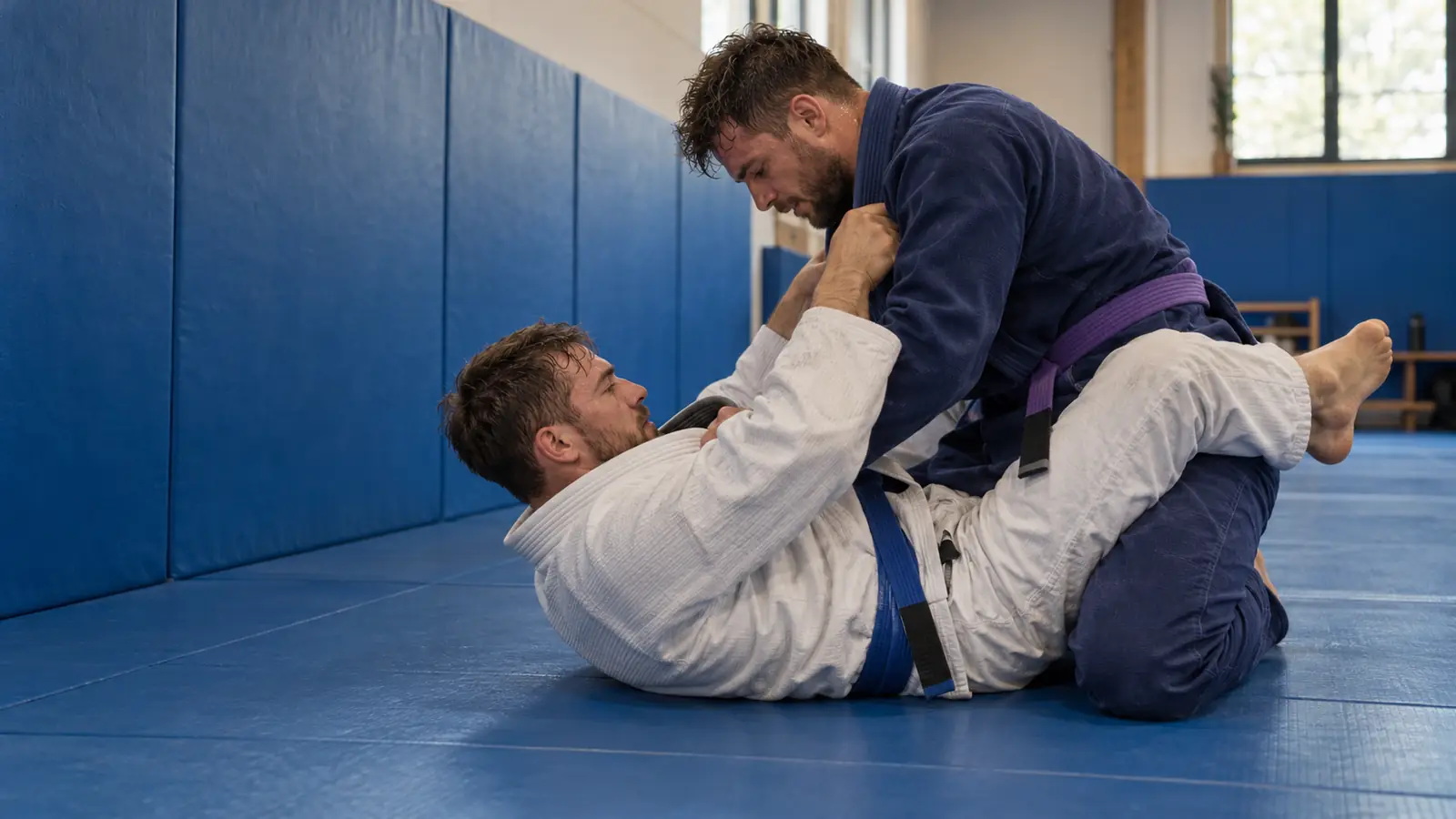 Двоє спортсменів BJJ у кімоно під час спарингу в партері